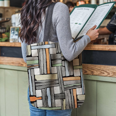 Mondrian Color Block Woven Tapestry Bag hanging on a woman's shoulder as she reads a menu at a restaurant counter.