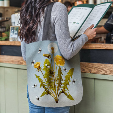 Dandelions and Bees Woven Tapestry Bag hanging on the shoulder or a woman reading a menu at a restaurant counter.